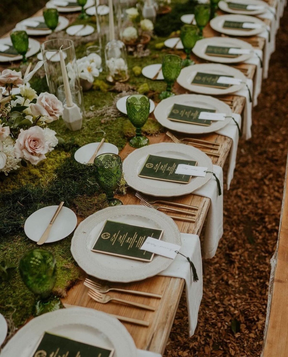10 Lace and Greenery Wedding Table Ideas to Try 4 A long wooden wedding table featuring a moss runner, roses, and green glassware.