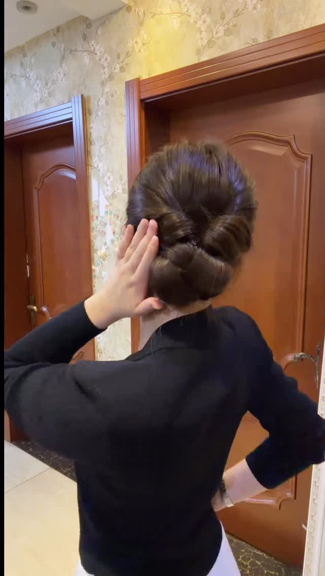 Woman showing a polished low chignon hairstyle while standing in front of wooden doors.