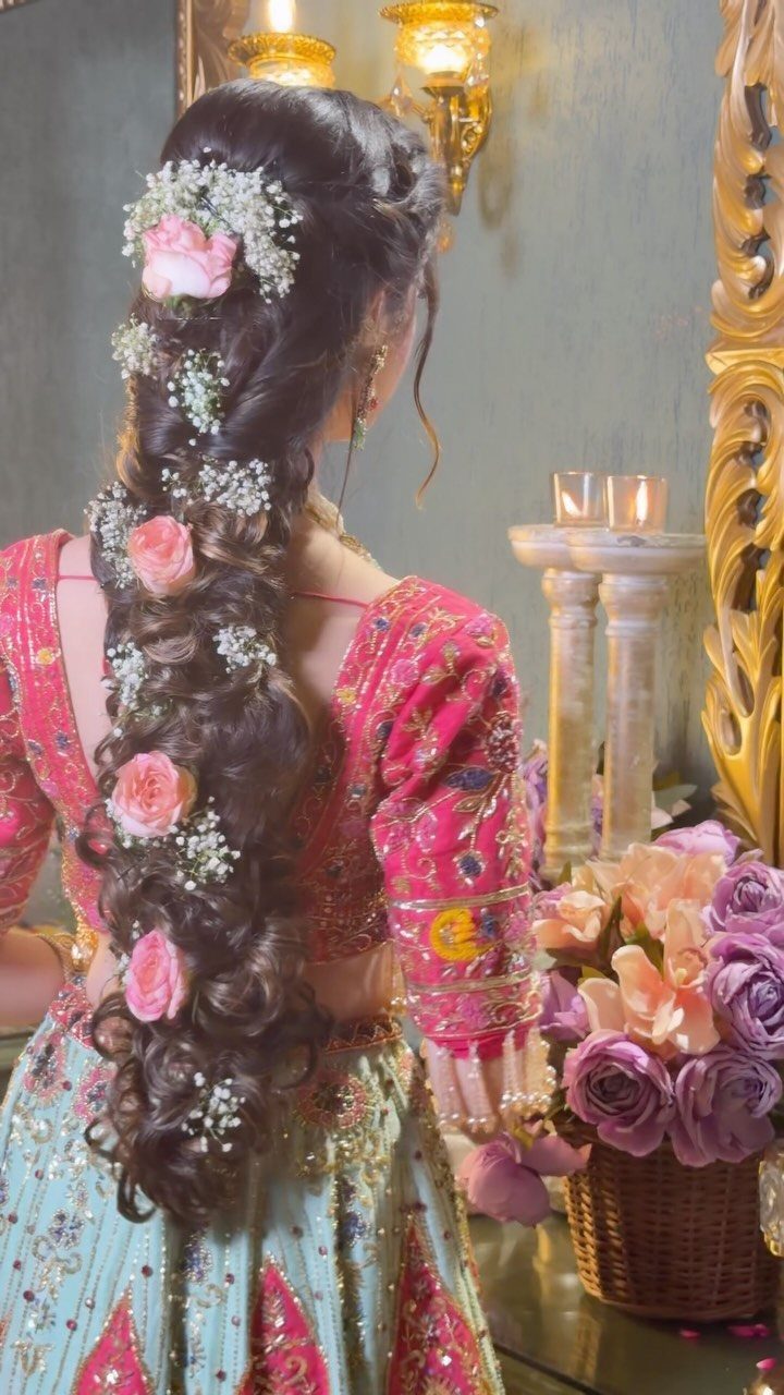 Woman with long, dark wavy hair styled in a braid with pink roses and white flowers.