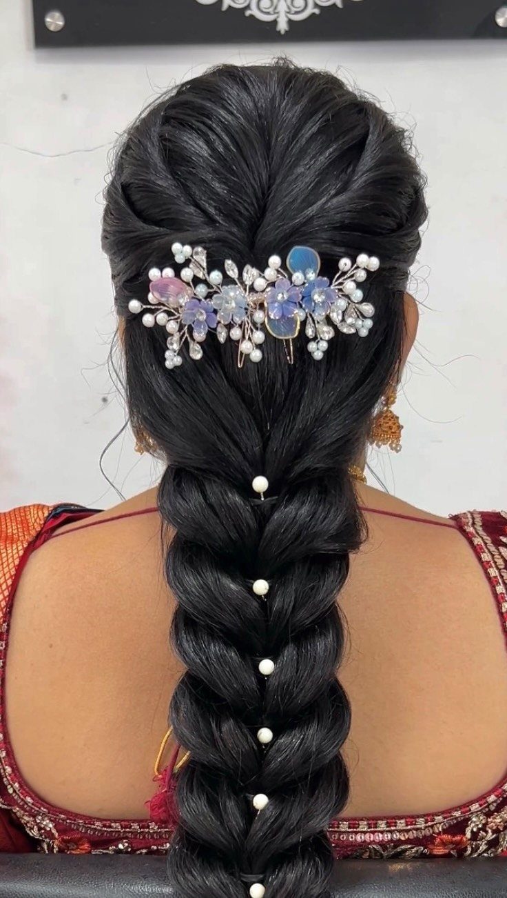 Dark braided hair decorated with a blue floral hairpiece and small white pearls.