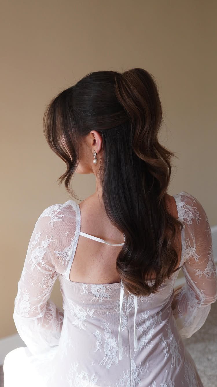 Woman with long dark hair in a half-up wedding hairstyle wearing a white lace dress.