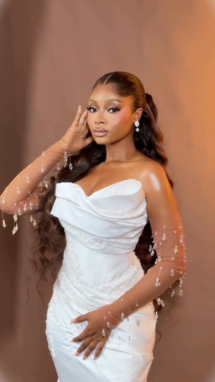 A woman with long, wavy dark hair styled in a sleek, voluminous high ponytail.