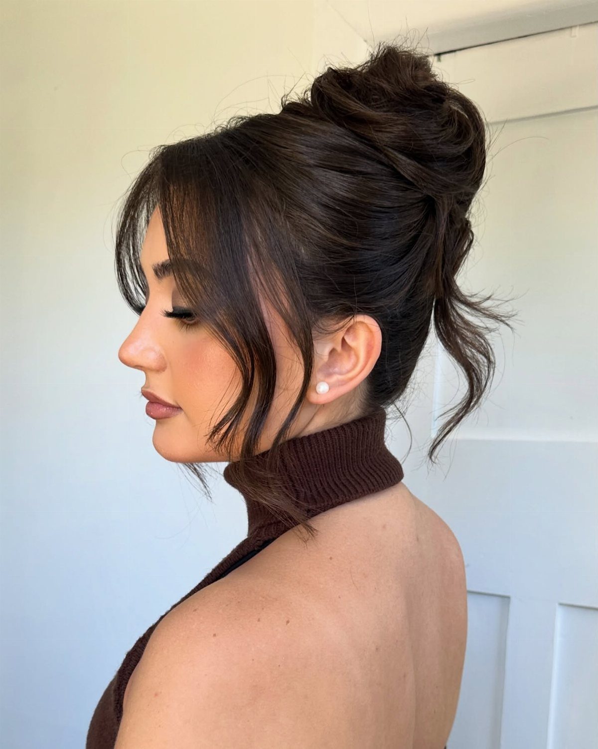 Woman with dark hair styled in a textured, voluminous knotted updo with face-framing strands.