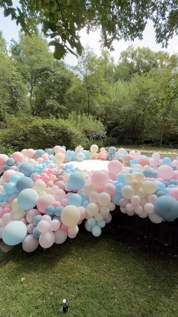 Pastel pink, blue, and cream balloons clustered together in an outdoor garden setting.