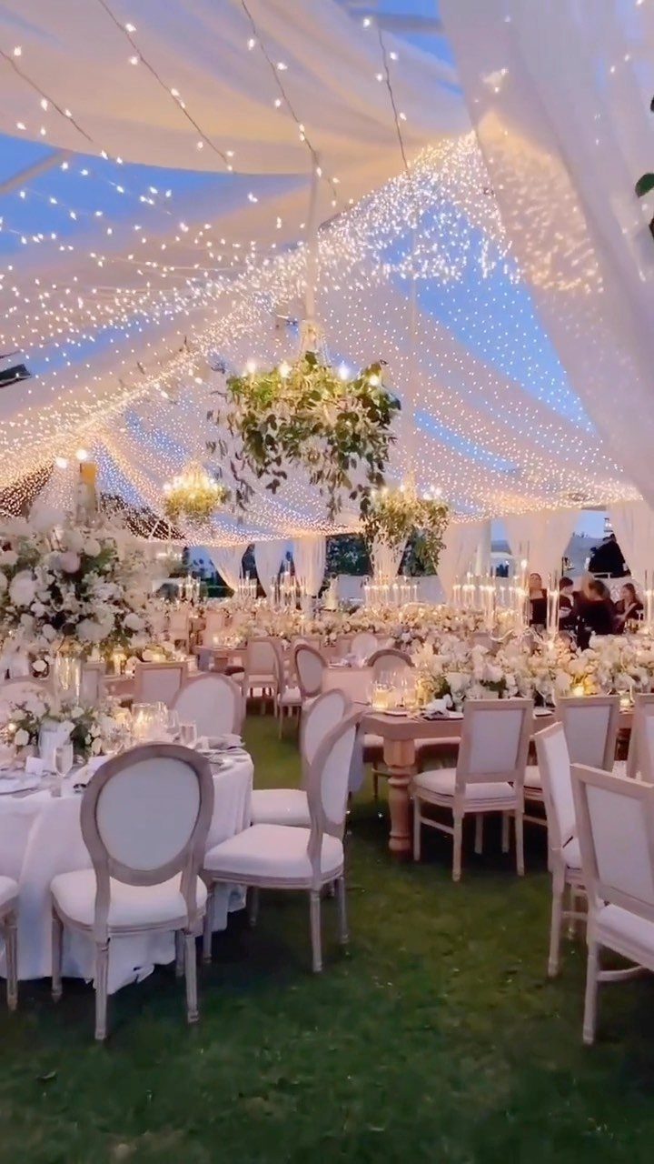 Fairy lights draped over white fabric canopy above wedding reception tables and chairs outdoors.
