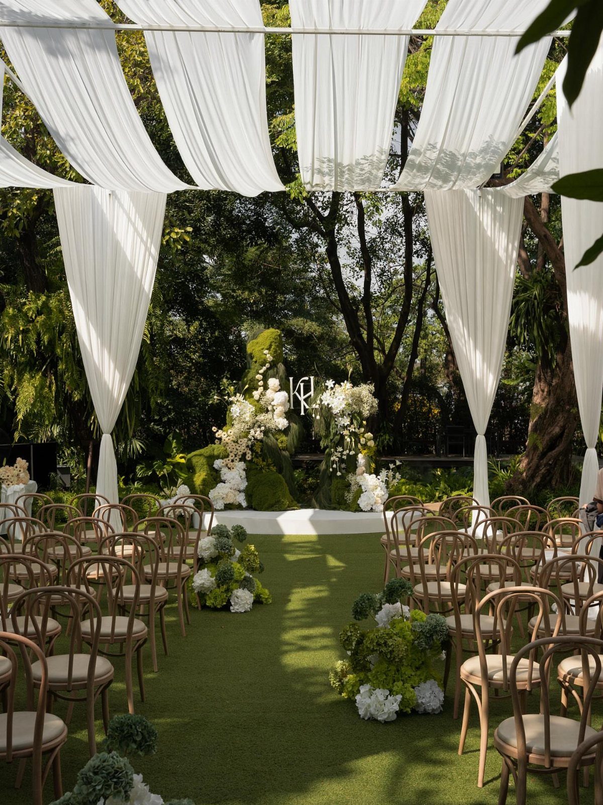 Wooden chairs arranged on a green lawn under white fabric draping in a garden.