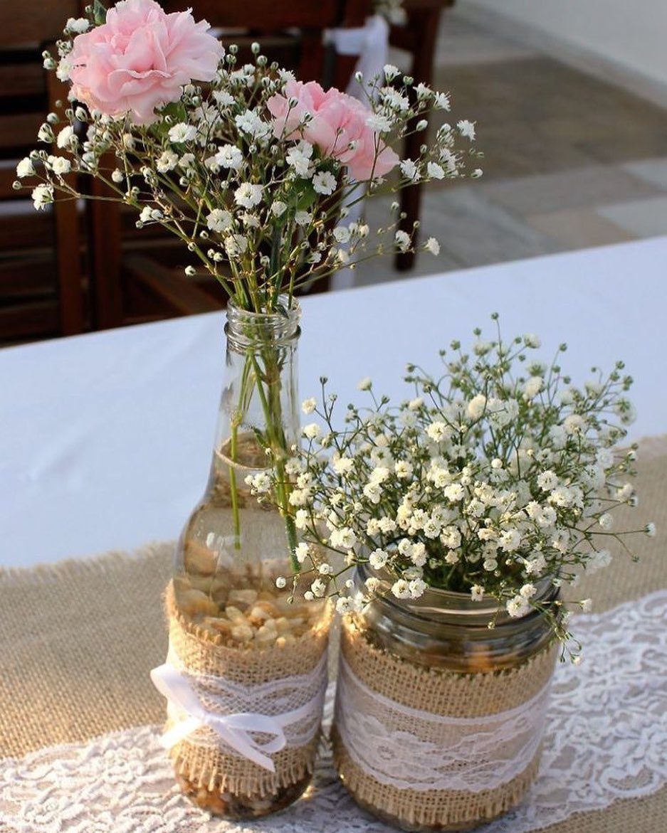 Glass mason jar and bottle wrapped in burlap and lace holding baby's breath and pink carnations.
