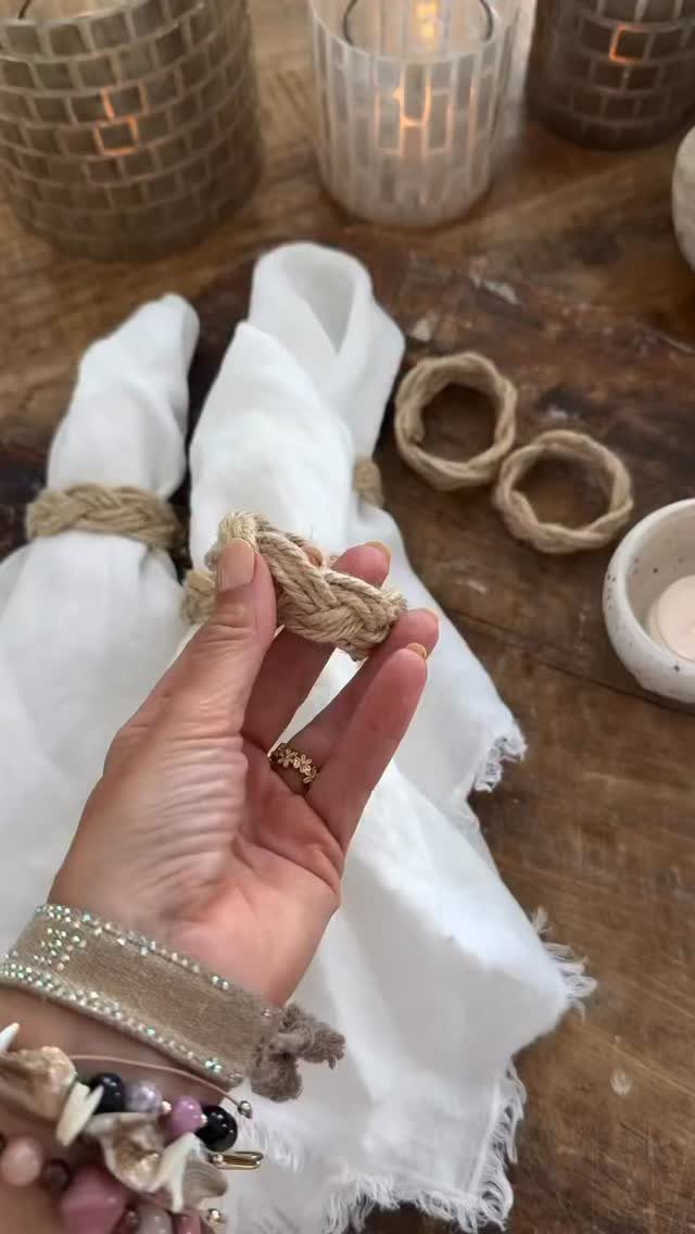 A hand holding a jute rope napkin ring over white linens on a wooden table.
