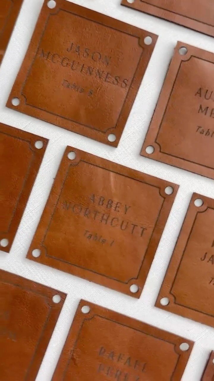 Brown leather place cards with names and table numbers arranged on a white surface.