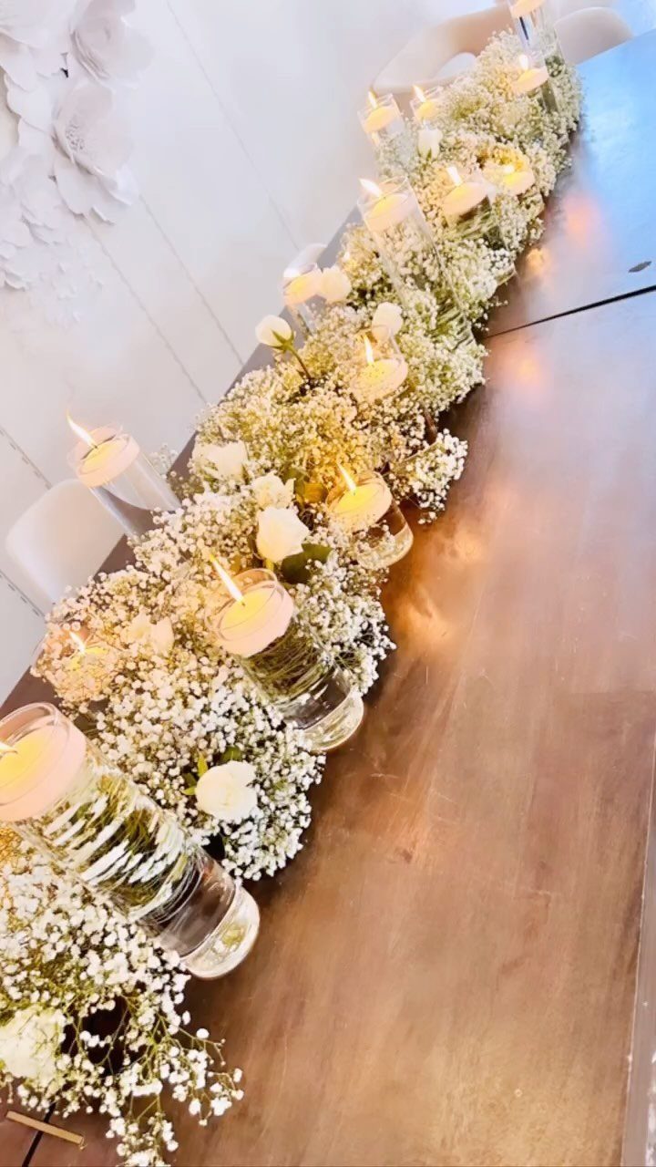 White baby's breath flowers and lit tea light candles arranged as a long table centerpiece.