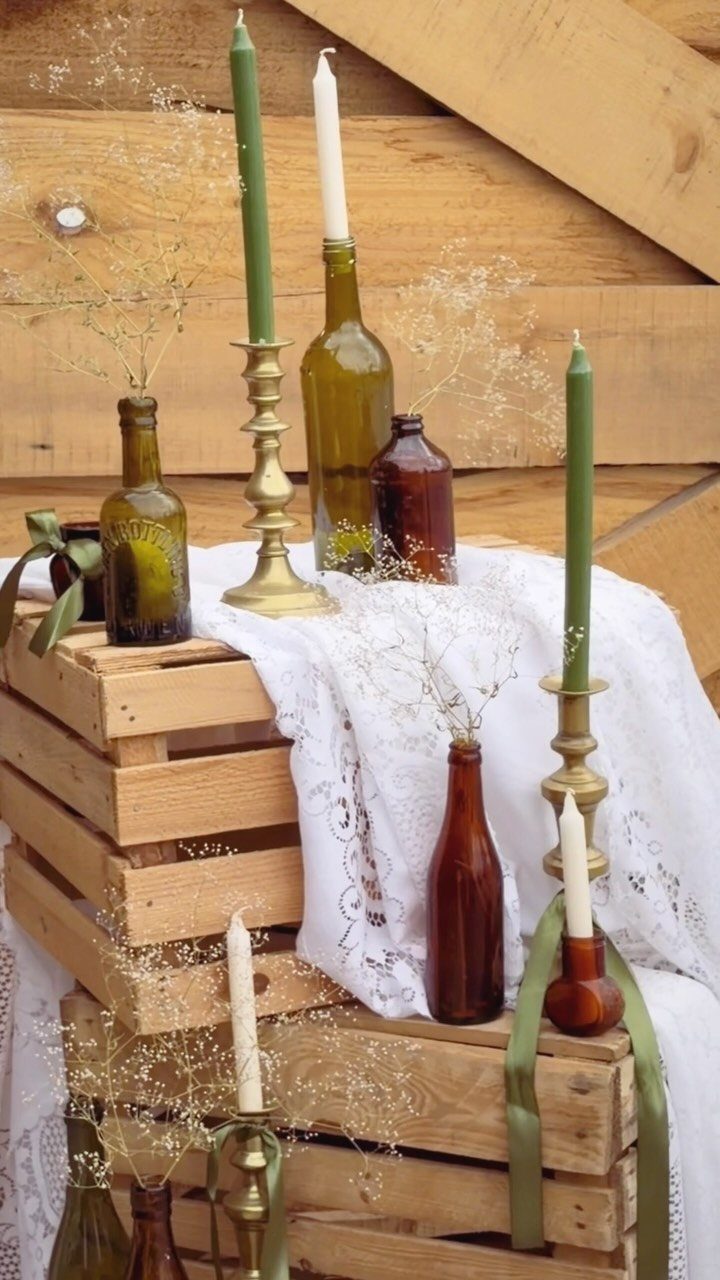 Glass bottles and taper candles arranged on wooden crates covered with white lace cloth.