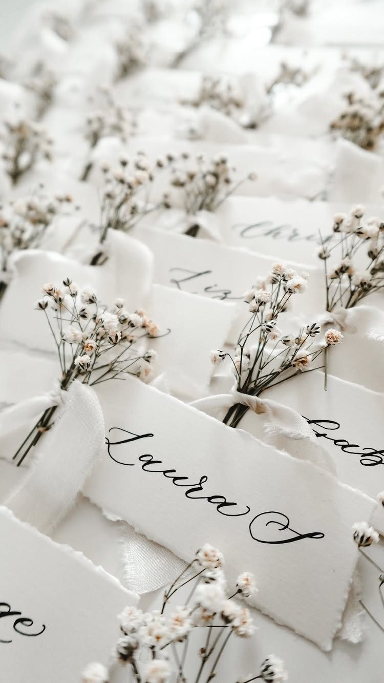 Calligraphed white paper cards decorated with small dried flowers arranged in rows.