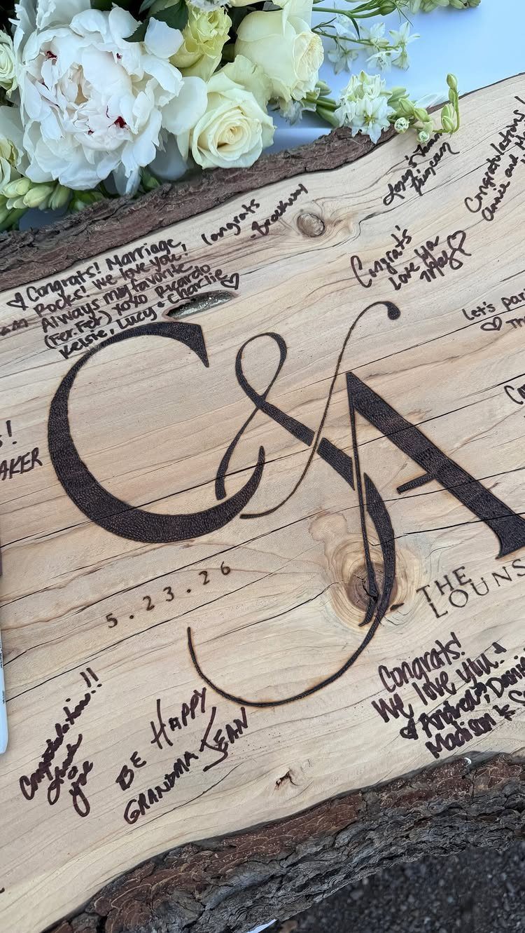 A rustic wooden slab guest book with handwritten messages and white flowers in the background.