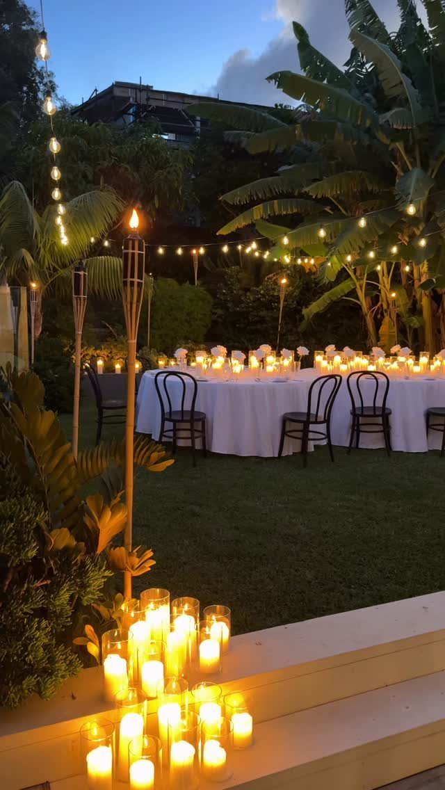 Simple Garden Wedding Reception Outdoor: 14 Stylish Ideas to Copy 13 A long wedding table set outdoors under string lights with glowing candles in the foreground.