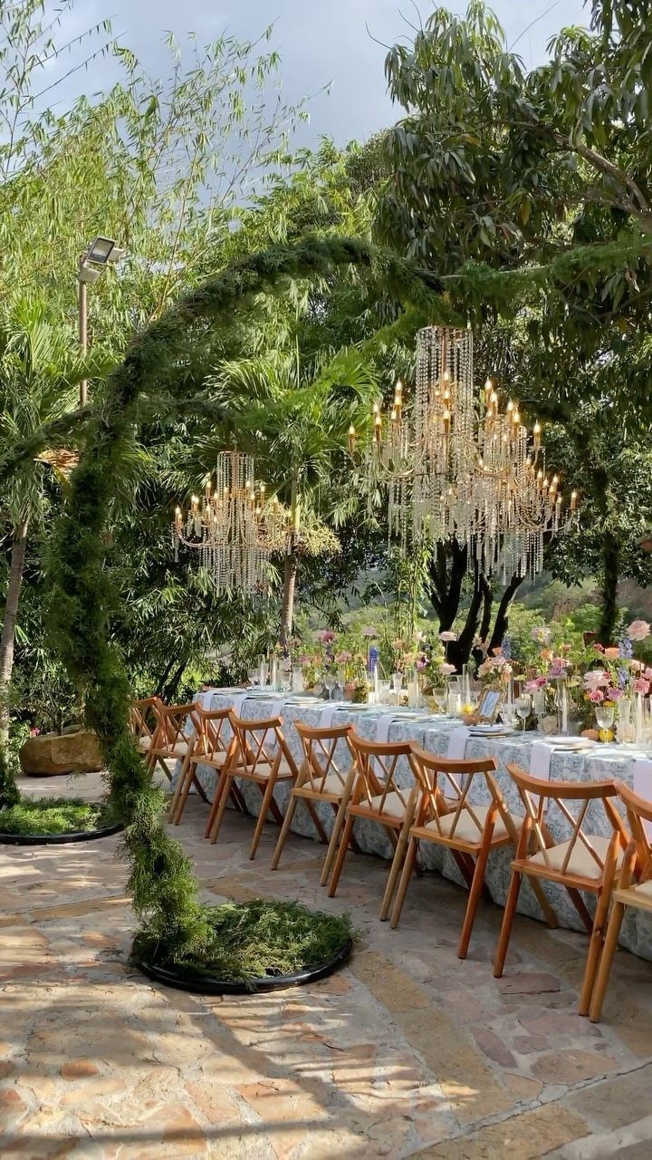 Simple Garden Wedding Reception Outdoor: 14 Stylish Ideas to Copy 11 Long wedding reception table with wooden chairs and hanging crystal chandeliers under green trees.