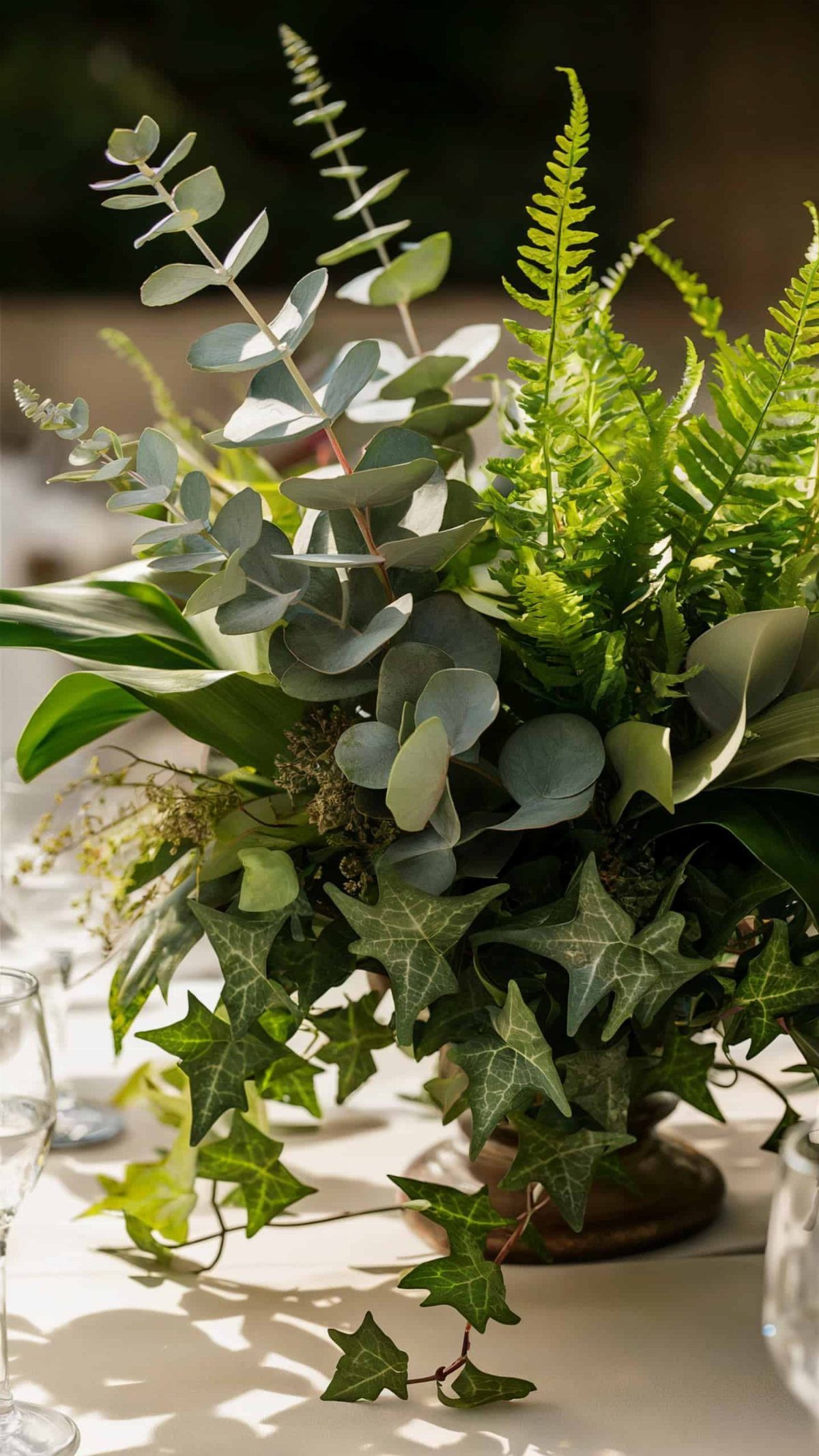 8 Simple Wedding Centerpieces for Budget-Friendly Tables 8 Greenery arrangement with eucalyptus, ferns, and ivy in a vase on a white table.