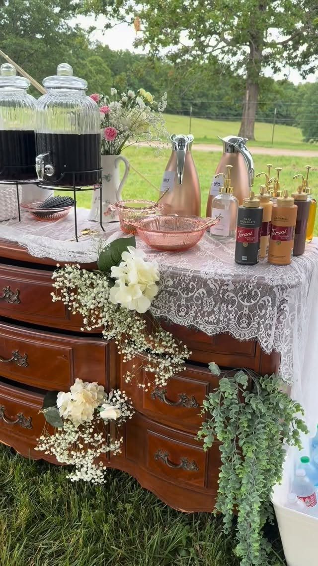 11 Thrifted Wedding Decor Ideas to Steal for Real Budgets 8 A wooden dresser decorated with lace and flowers serving as an outdoor wedding beverage station.