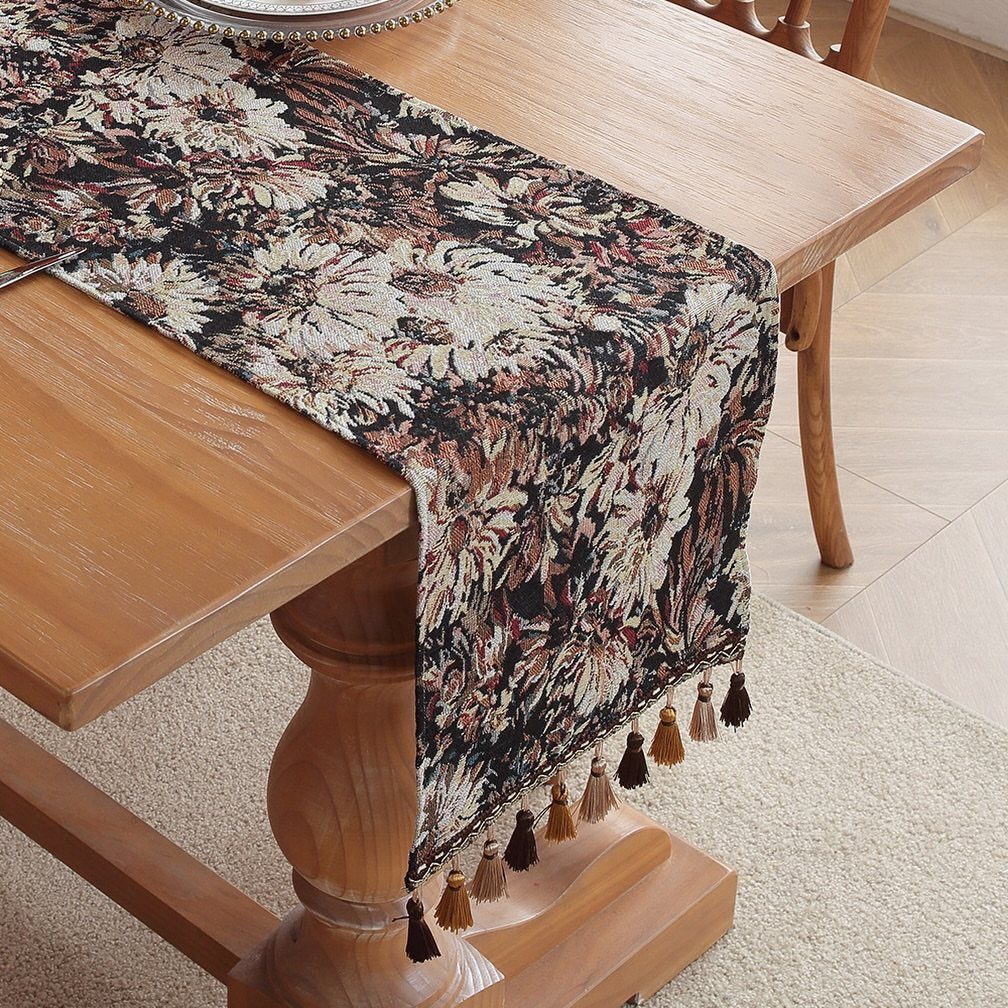 11 Thrifted Wedding Decor Ideas to Steal for Real Budgets 10 A floral patterned tapestry table runner with tassels draped over a light wooden dining table.