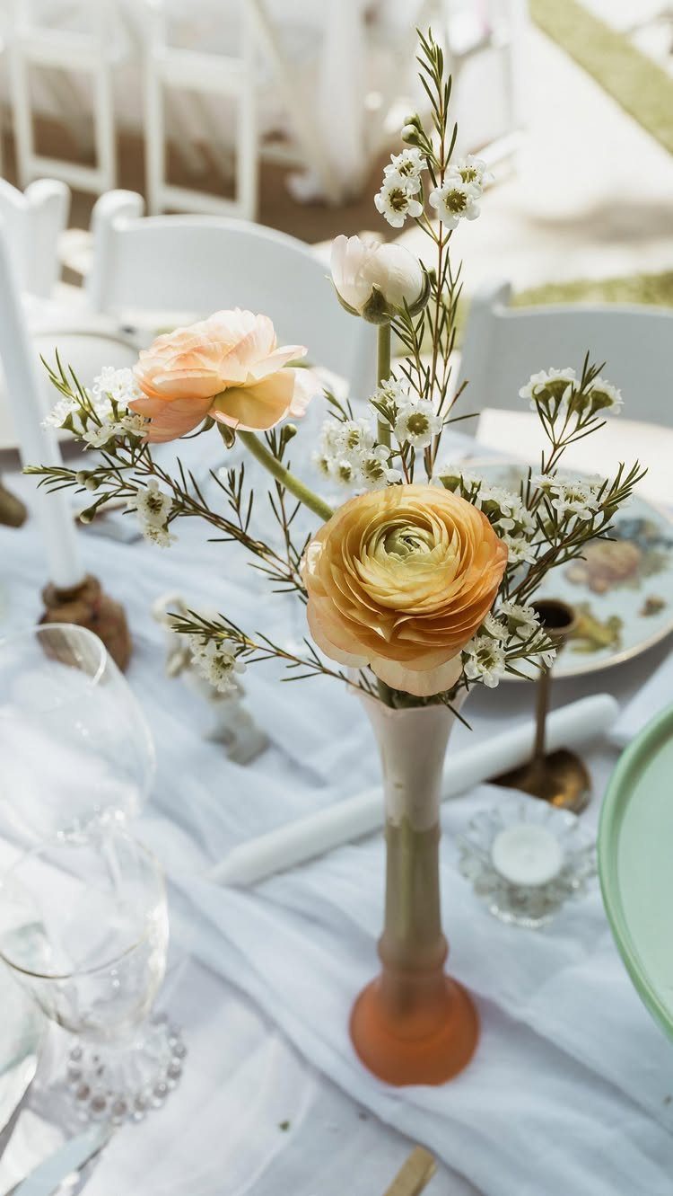 11 Thrifted Wedding Decor Ideas to Steal for Real Budgets 5 A peach and cream vase containing peach ranunculus and small white flowers on a wedding table.