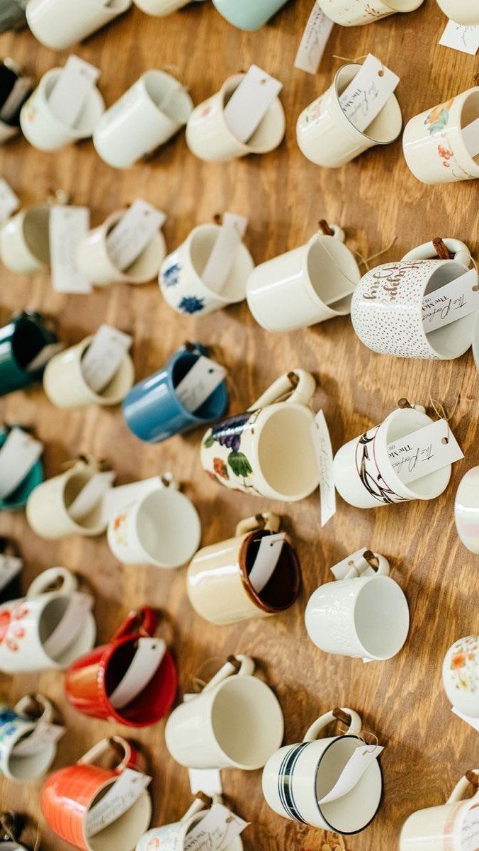 11 Thrifted Wedding Decor Ideas to Steal for Real Budgets 3 Mismatched ceramic mugs with white gift tags hanging on a wooden wall.