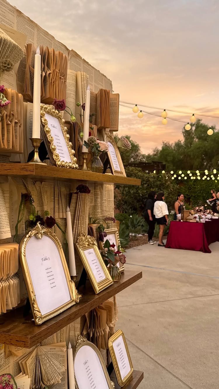 Old books with fanned pages decorate wooden shelves alongside gold frames and white taper candles.