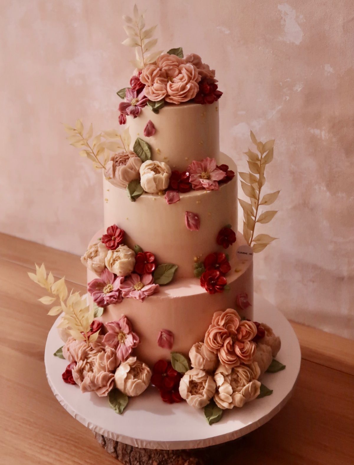 A three-tier peach cake adorned with intricate buttercream flowers and gold leaf accents.