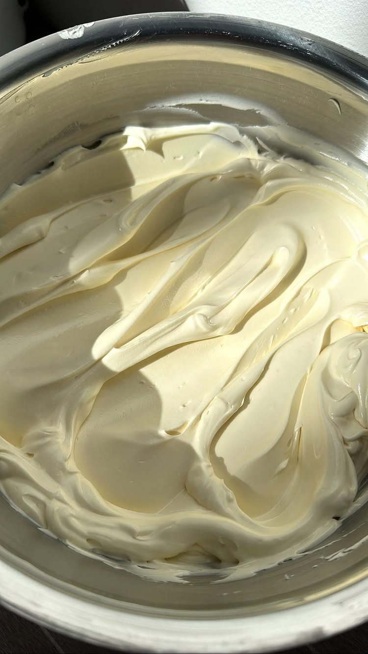 Swirled off-white buttercream frosting inside a large stainless steel mixing bowl.