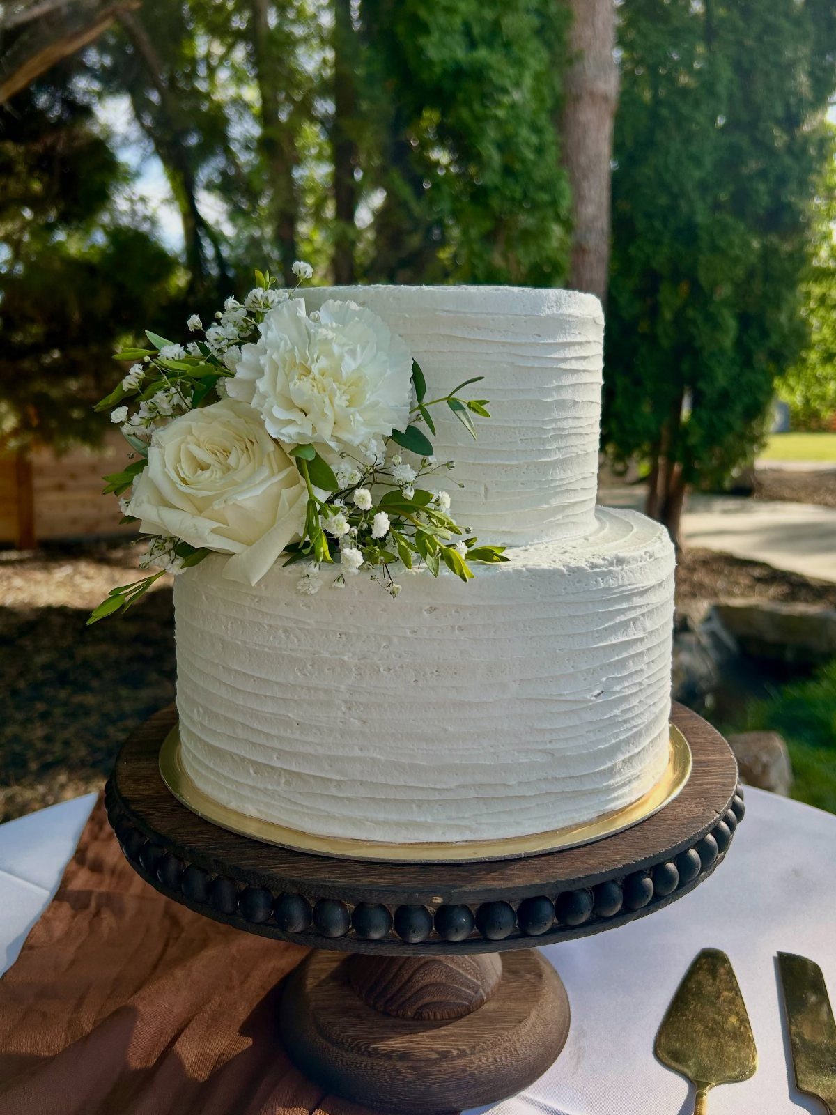 Two-tier white textured buttercream wedding cake decorated with white roses and greenery on a wooden stand.