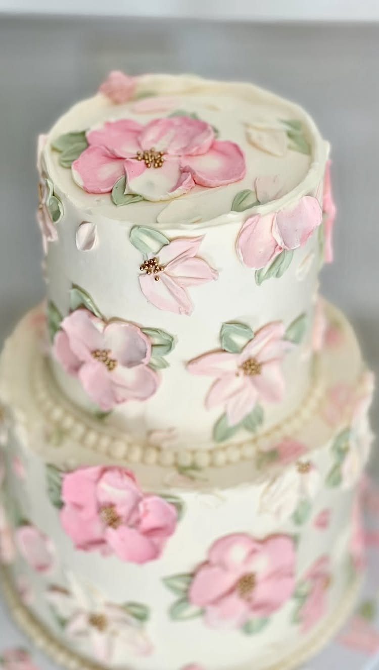 Two-tier white wedding cake decorated with pink buttercream flowers and green leaves.