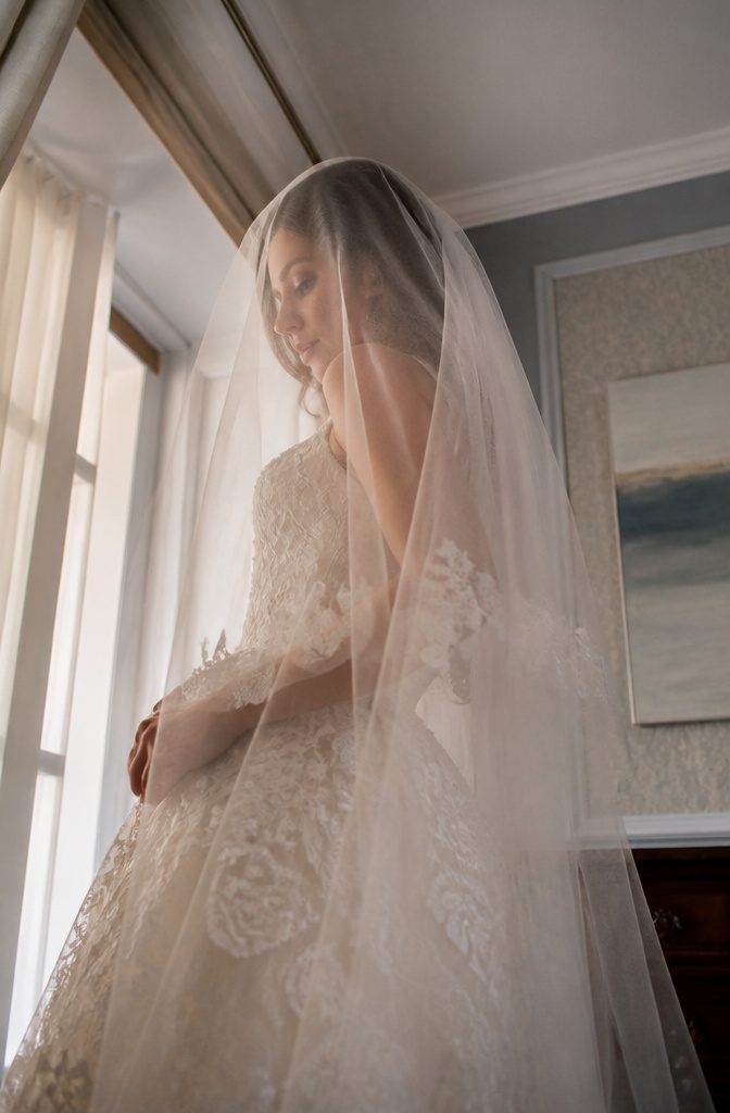 Bride holding her veil above her face in a dim setting.