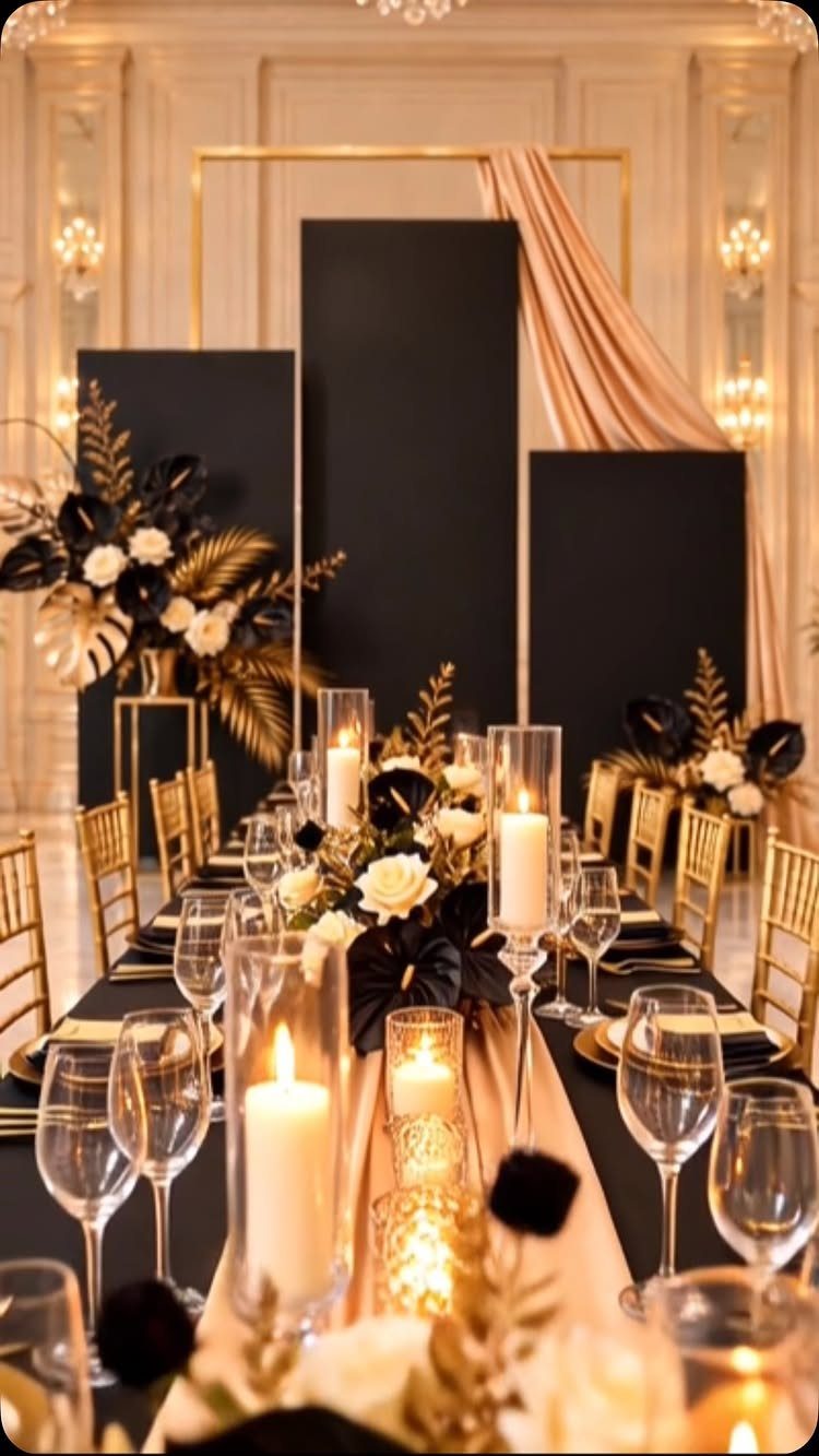 A formal banquet table decorated with black linens, gold chairs, white roses, and glowing candles.