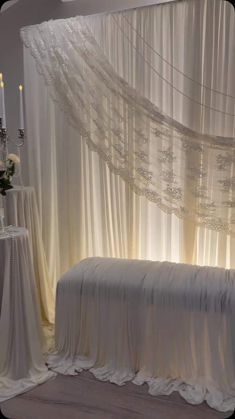 White draped fabric backdrops with a large scalloped lace overlay and white tablecloths.