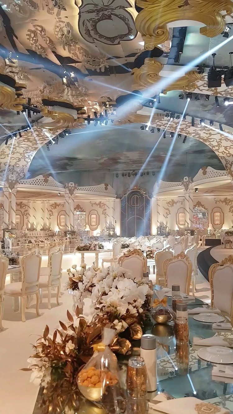 Ornate ballroom with gold ceiling details, murals, classical columns, and elegant wedding table settings.