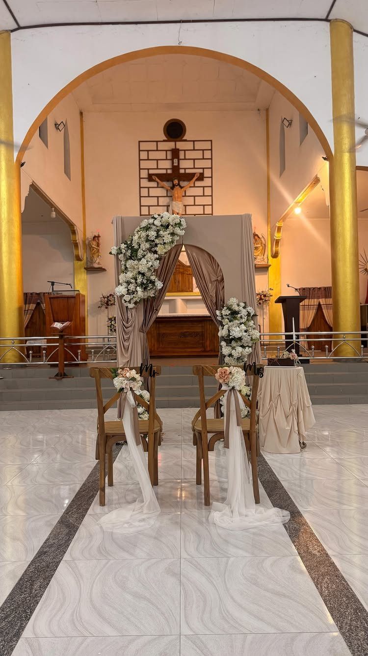 Two decorated wooden chairs facing a floral arch inside a church sanctuary.