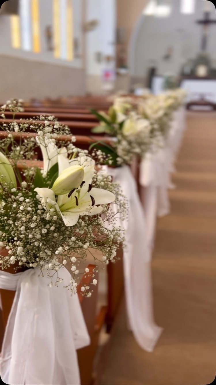 White lilies and baby's breath decorate wooden church pews with flowing white fabric.