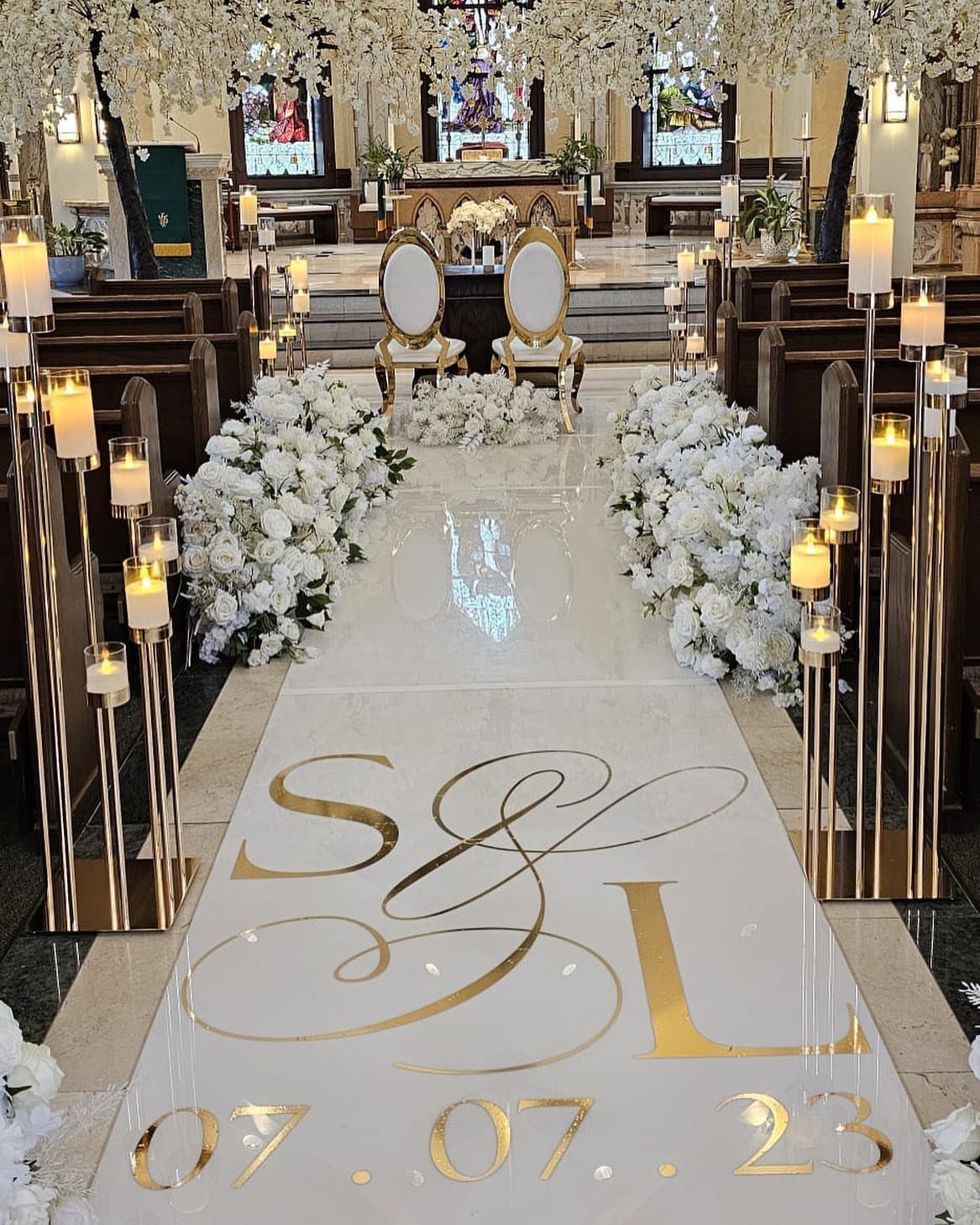 White aisle runner with gold lettering and large white flower arrangements in a church aisle.