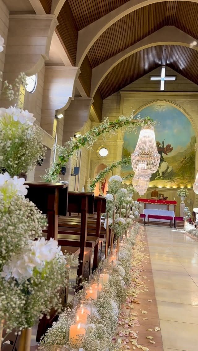 White flowers and glowing tealight candles lining a church aisle next to wooden pews.