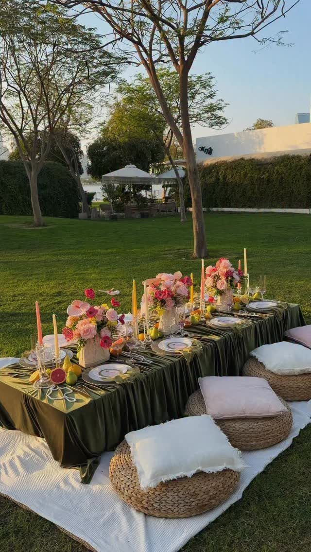 20 Wedding Decor DIY Ideas for Ceremony and Reception 10 A decorated outdoor dining table with floral arrangements, candles, and floor poufs on a lawn.