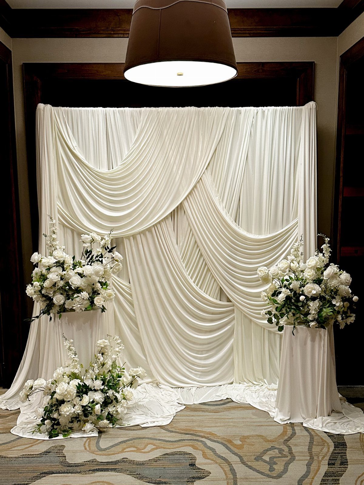 20 Wedding Decor DIY Ideas for Ceremony and Reception 12 White fabric draped in elegant swags serving as a wedding backdrop with floral arrangements.