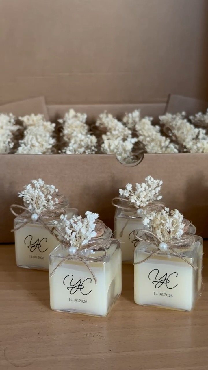 20 Wedding Decor DIY Ideas for Ceremony and Reception 4 Four small square glass jar candles decorated with dried flowers and twine on a wooden surface.