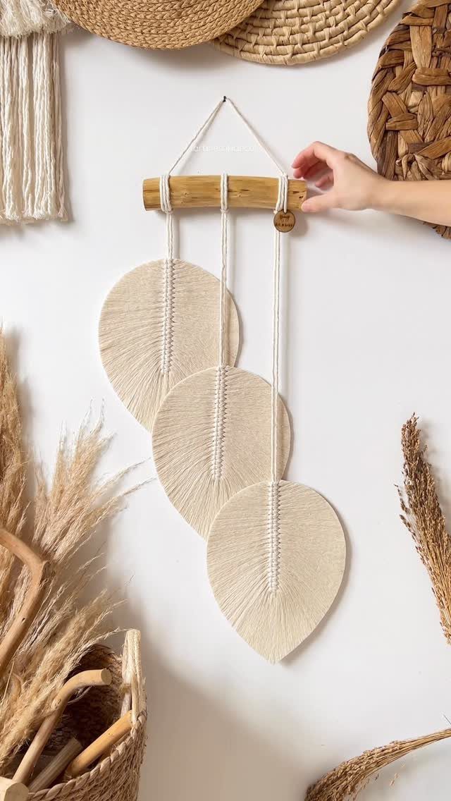 20 Wedding Decor DIY Ideas for Ceremony and Reception 20 A hand holds a wooden rod with three large cream macrame leaf decorations hanging against a wall.