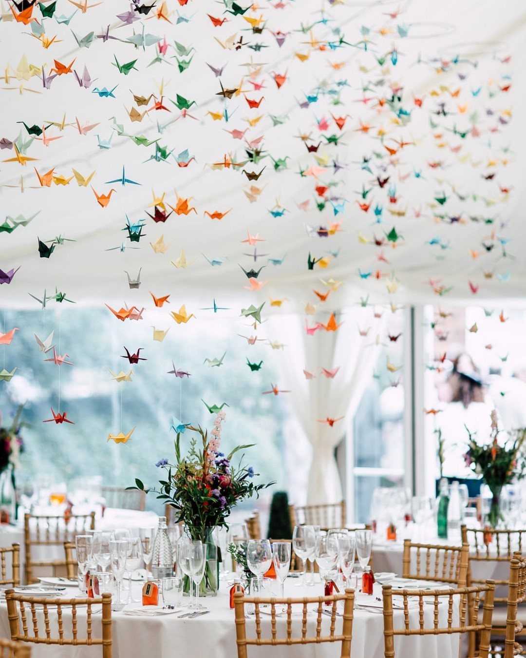20 Wedding Decor DIY Ideas for Ceremony and Reception 7 Colorful origami cranes hanging from strings above a decorated wedding reception table.