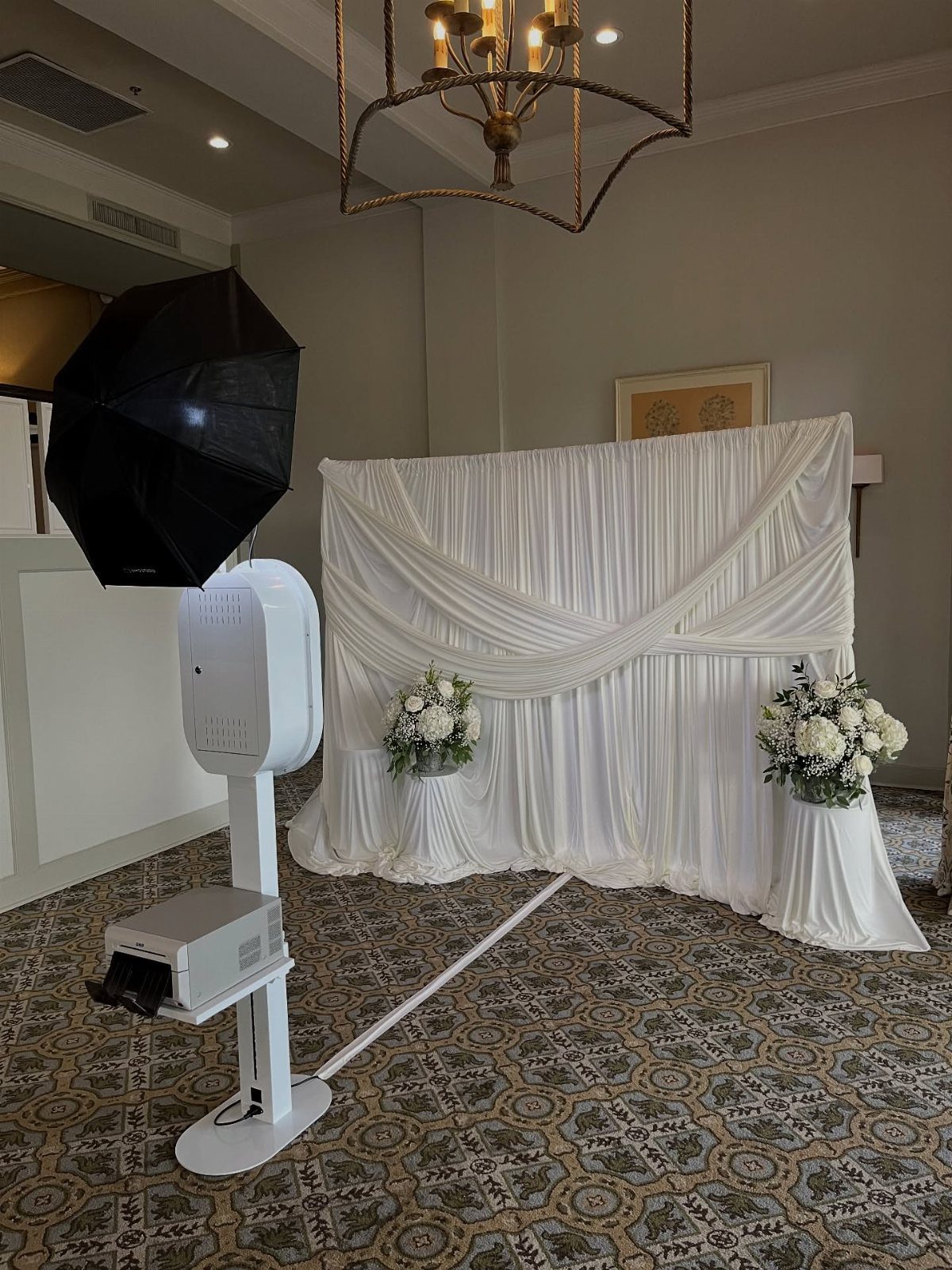 20 Wedding Decor DIY Ideas for Ceremony and Reception 3 White draped fabric backdrop with floral arrangements and a photo booth kiosk setup.