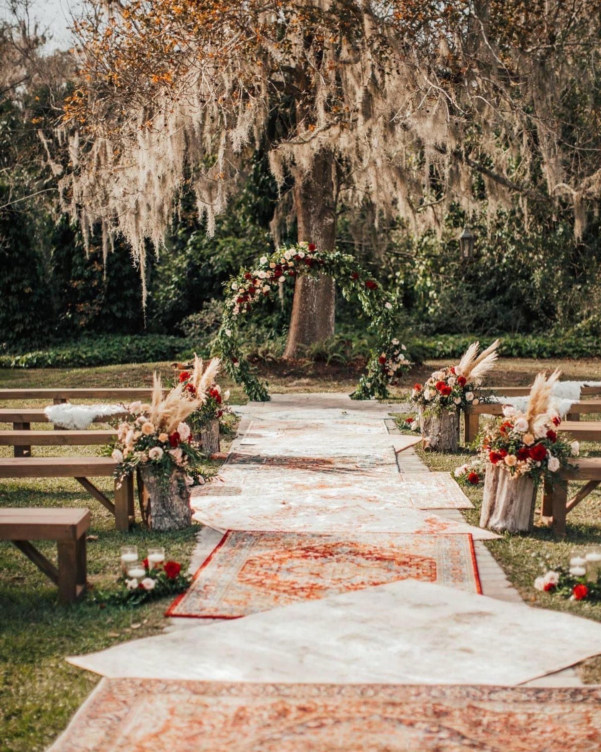 20 Wedding Decor DIY Ideas for Ceremony and Reception 15 Patterned rugs laid on grass forming a wedding aisle leading to a floral arch.