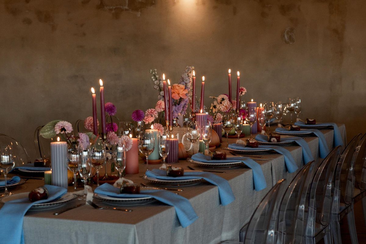 22 Wedding Decor Garden Theme Ideas for Every Reception Style 12 A long dining table decorated with colorful taper candles, blue linens, and assorted glassware.