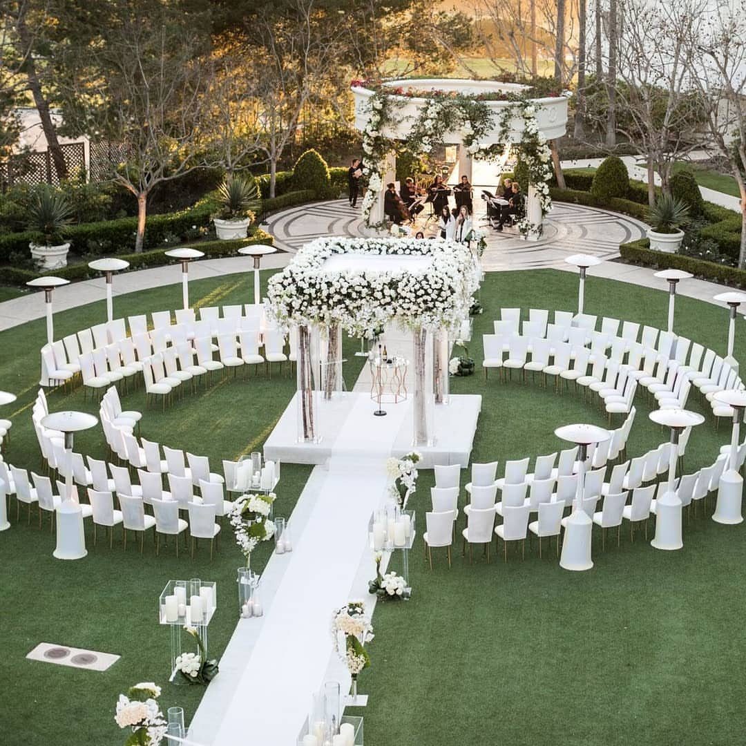 22 Wedding Decor Garden Theme Ideas for Every Reception Style 6 White wedding chairs arranged in large circular patterns on a green lawn around a floral canopy.