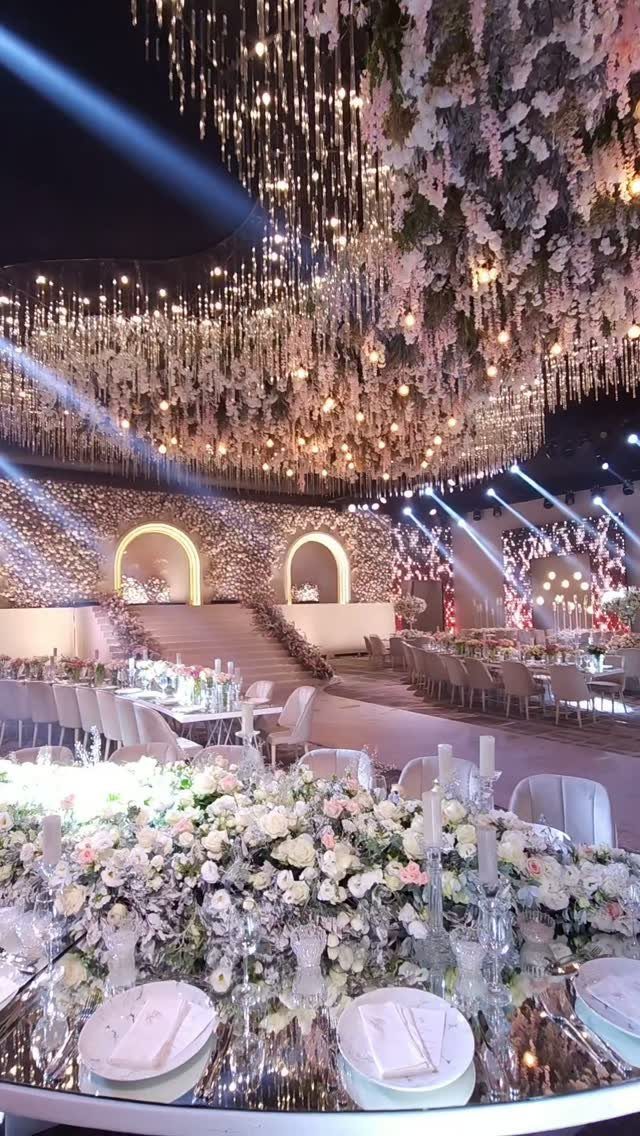 22 Wedding Decor Garden Theme Ideas for Every Reception Style 3 Floral arrangements and hanging lights create a lush indoor garden setting in a large banquet hall.