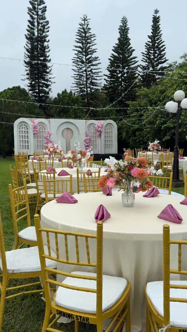 22 Wedding Decor Garden Theme Ideas for Every Reception Style 17 Round wedding tables with pink napkins and floral centerpieces set on a green lawn.