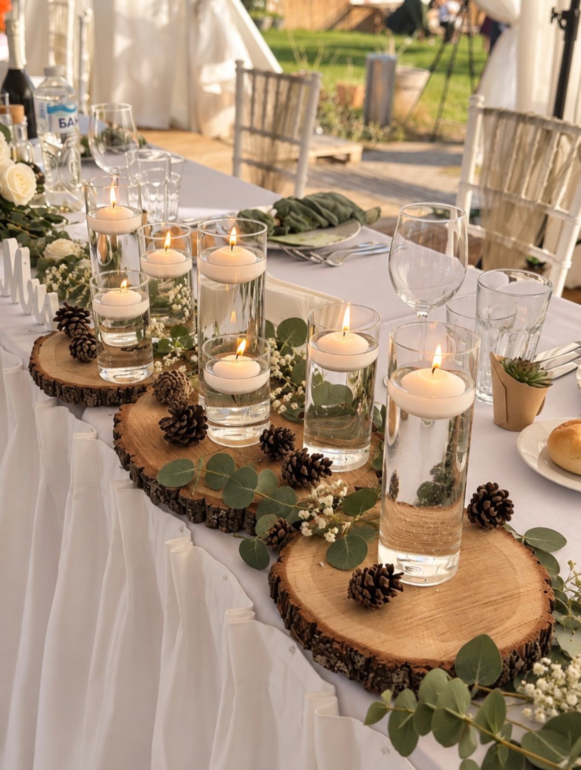 22 Wedding Decor Garden Theme Ideas for Every Reception Style 13 Floating candles in glass cylinders arranged on wood slices and eucalyptus leaves on a wedding table.