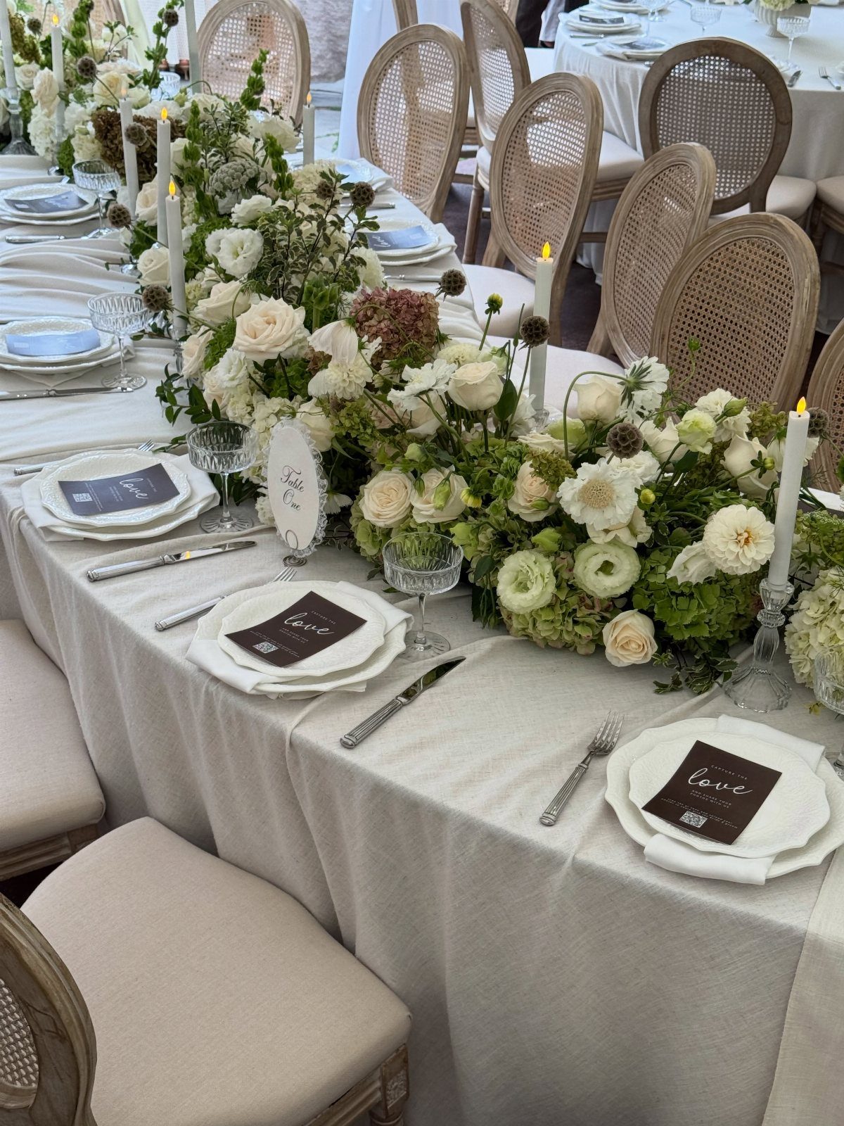 22 Wedding Decor Garden Theme Ideas for Every Reception Style 4 White floral arrangements with roses and greenery decorate a long wedding reception table with candles.
